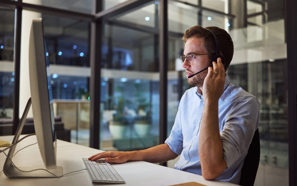 Side view of a man holding a headset while on a call looking at computer screen