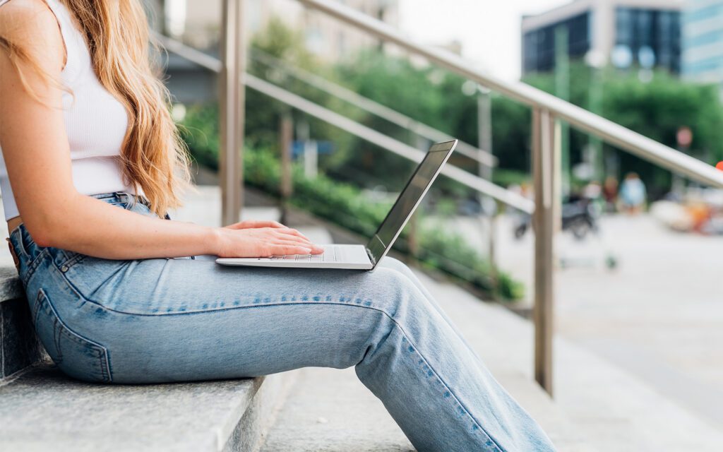 Side view of a woman sitting down on stairs working on laptop